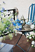 Unusual, antique teapots on silver tray on blue-painted garden chair; terrace with floral balustrade