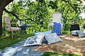 Stylish picnic area in shades of pastel blue and beige with inviting cushions, blankets and Rococo chairs next to garden table