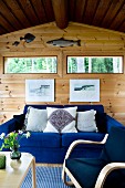 Comfortable, electric blue sofa and armchair in simple wooden house; two window slits and angling trophies above sofa