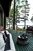 Wooden terrace with comfortable terrace furniture, candle arrangement and wonderful view of lake between tall pines and birches