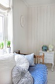 Vintage daybed with blue and white throw and soft cushions below window in sunny room