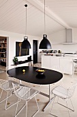 Retro hanging lamps above a dining table with black top and chairs with white metal frames in a functional kitchen