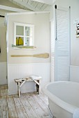 White slatted doors, mirror in window frame, maritime decor and vintage bench in country-house bathroom