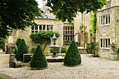 Conical, topiary bushes around fountain in courtyard of English stately home