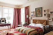 Butterfly collection on wall above wicker headboard of double bed, striped textiles and antique dressing table in front of lattice windows