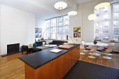 Städtische, offene Designer-Wohnung im Retrostil mit Lampionleuchten über schwarzer Küchenarbeitsplatte und weißem 60er Jahre Essplatz