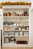A variety of glassware, earthenware and crockery stored in an open white wooden shelf