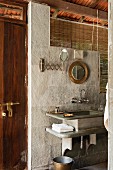 Waschtisch aus Stein an Wand mit hellgrauen Steinplatten und Bambusrollo vor fensterartiger Öffnung
