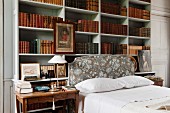 Double bed in front of open-fronted shelving holding antiquarian book volumes