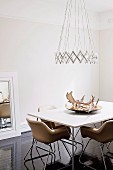 Designer pendant lamp above dining table with antlers in dish and fifties-style leather chairs on dark, glossy wooden floor