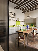 Large wooden table and chairs in kitchen with pale green cupboard doors and apple-green splashback