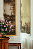 Upturned wine glasses on small antique table and bouquet of roses in front of large landscape painting in elegant hotel lobby