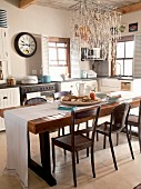 Rustic, wooden dining table with white table runner and assortment of chairs under a light with a nautical light fixture in a country kitchen