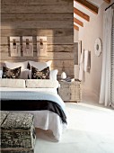 An assortment of decorative pillows and bolsters on double bed against a rustic, wood plank wall serving as a room divider and floor to ceiling opening to the en suite