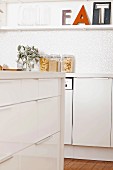 Detail of modern white kitchen with drawer unit, decorated wall-mounted shelf and full storage jars with lids on worksurface
