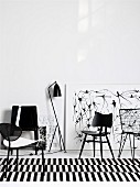 Black chairs from various eras on black and white striped rug in front of drawings leaning on wall