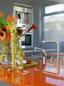 Designerküche mit orangefarbener Arbeitsplatte und Blumenstrauß mit Callas in Glasvase