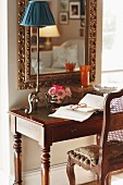 Reading area with antique bureau and wooden chair below gilt-framed mirror