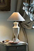Table lamp with marble base on grey, vintage bedside table; heavy, gathered curtain in background