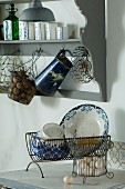 Old wire baskets and vintage metal jug hanging from grey, nostalgic kitchen wall rack; antique crockery in draining rack in foreground