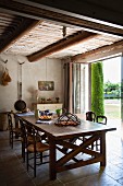 Large wooden table and rush bottom chairs under wooden ceiling of restored country house in southern France