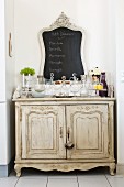 Collection of glass carafes and chalkboard on antique, shabby-chic cabinet in niche