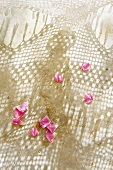 Rose petals on sand and pattern of light and shade through crocheted hammock