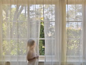 Kleinkind in Windel steht hinter Gardine am Fenster