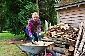 Young woman loading a wheelbarrow with chopped firewood