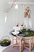 Nordic Advent arrangement with champagne, confectionery, popcorn and lit candles in bottles on tray table draped with moss