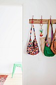 Various handbags hanging on coat rack on white wall next to open doorway