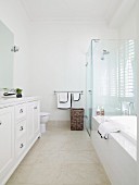 High-ceilinged bathroom in elegant, white, country-house style with glass shower partition and stone-coloured tiled floor
