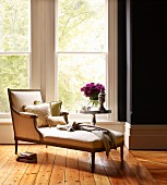 Inviting reading area in front of French windows with scatter cushions on antique chaise longue and side table