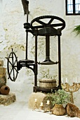 Vintage olive press and various candlesticks on floor against wall of Mediterranean farm house