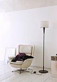 Stack of clothes on comfortable, leather swivel chair and standard lamp in informal artist's apartment with white furnishings and surfaces