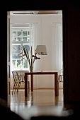 View of modern dining table and designer pendant lamp in classic setting through open doorway