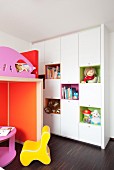 Contemporary, child's bedroom with white fitted cupboards, colourful shelving modules and brightly coloured loft bed on dark wooden floor