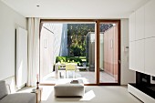 Blick von Designer Wohnzimmer durch Terrassenfenster auf Outdoormöbel in patioartigem Innenhof
