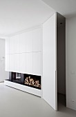 Storage space with open door next to fitted cupboards with integrated fireplace and firewood store