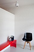 Corner of white interior with black designer chair and red metal bench