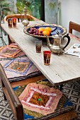 Oriental teapot and glasses on wooden table and colourful seat cushions on wooden bench