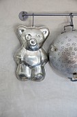 Bear-shaped cake tin and old metal colander hanging from butchers' hooks on metal rod