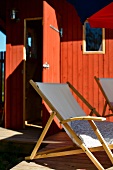 Deckchairs on terrace in front of wooden house painted rust red