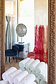 Rolled towels against bathroom mirror with designer chairs and lamps reflected in background