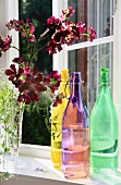 Colourful swing-top bottles and vase of flowers on window sill