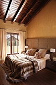 Schlafzimmer in Naturtönen mit breit gepolstertem Kopfteil und Fell-Accessoires auf dem Doppelbett