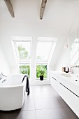 Modern bathtub opposite washstand with integrated sink in designer bathroom with dormer window