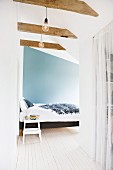Attic bedroom with bed against blue wall and pale wooden floor