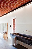Stone, trough-style washstand against wall in open-plan foyer with brick ceiling