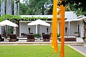 Lengths of orange fabric hanging over lawn; loungers and parasols on terrace with roofed area in background